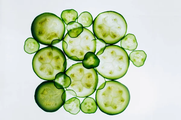 Fatias translúcidas verdes de pepino no fundo da luz branca brilhante close-up. discos transparentes de legumes. textura dos padrões caleidoscópicos na macro — Fotografia de Stock