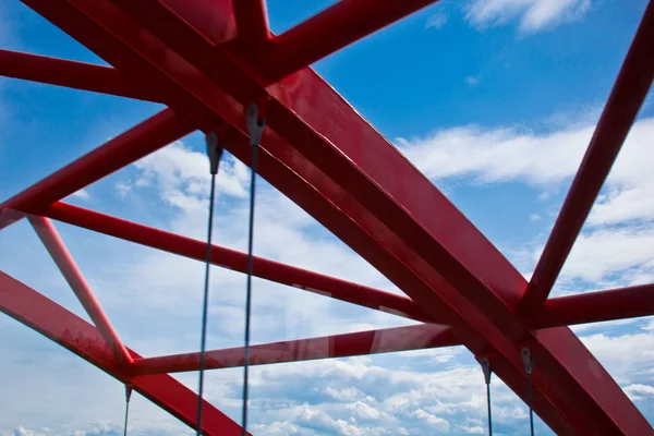 Raios de uma ponte arqueada vermelha close-up contra um céu azul. textura da treliça das partes da ponte de aço. transição cortada para o outro lado — Fotografia de Stock