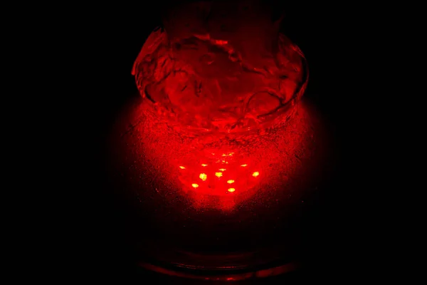 a glass hookah flask filled with bubbling water and smoke glows in the dark in red. luminescence in darkness