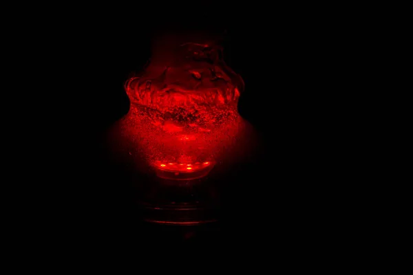 Köpüren su ve duman la dolu bir cam nargile şişesi kırmızı karanlıkta parlıyor. karanlıkta ışıltı — Stok fotoğraf