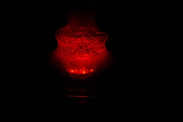 Köpüren su ve duman la dolu bir cam nargile şişesi kırmızı karanlıkta parlıyor. karanlıkta ışıltı — Stok fotoğraf