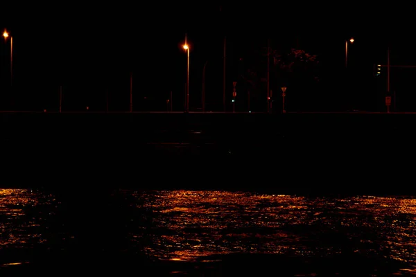 La lumière des lanternes de la ville se reflète dans l'eau la nuit. vagues sur la rivière — Photo