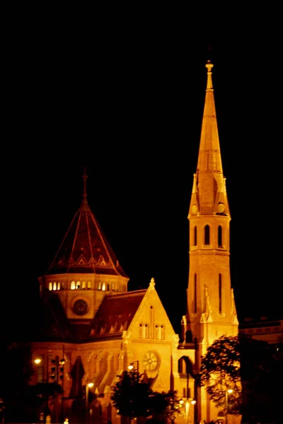 O edifício de alta torre no telhado brilha amarelo à noite. Cidade da noite. capela alta — Fotografia de Stock