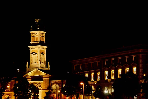 O edifício de alta torre no telhado brilha amarelo à noite. Cidade da noite. capela alta — Fotografia de Stock