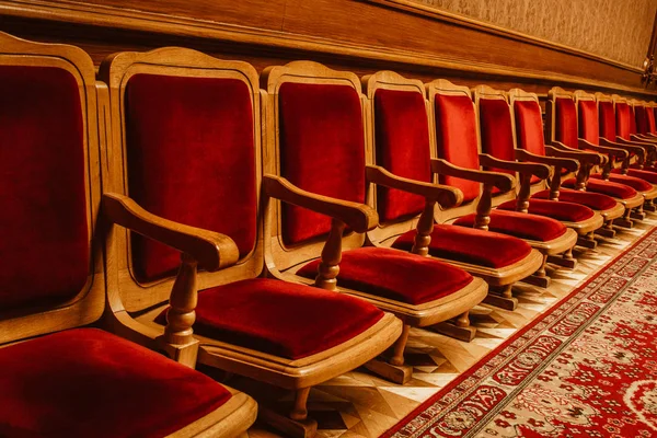 Una fila de sillas vintage de madera cubiertas de terciopelo rojo de pie contra una pared. sala en el teatro — Foto de Stock
