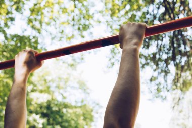bir spor atlet elleri açık bir gökyüzü ve yeşil yeşillik karşı eğitim zemin Pull-up için metal bir crossbar tutun. spor eğitimi açık havada. egzersiz birinci şahıs görünümü