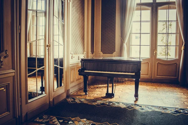 Un piano de cola clásico negro se encuentra en medio de una habitación de lujo junto a una ventana bajo la luz del sol. instrumento musical clásico, barroco interior — Foto de Stock