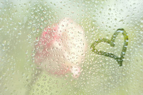 Finger-drawing a love symbol of a heart shape on a translucent sweated glass. raindrops of spring rain on the window close-up. blurred background copy space