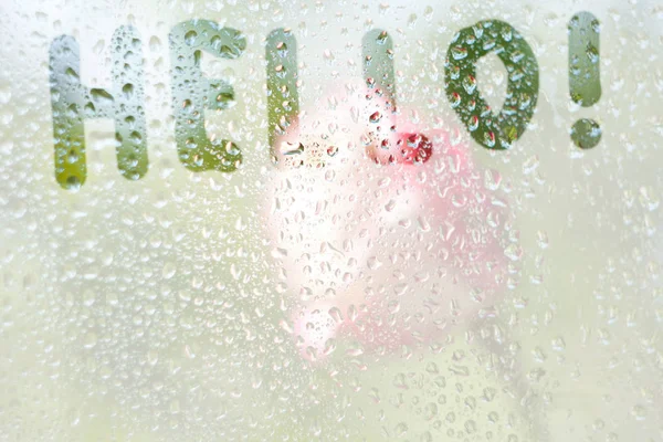 Finger-shaped drawing of the stripes of the word hello on translucent fogged glass. raindrops of spring rain on the window close-up. blurred background copy space