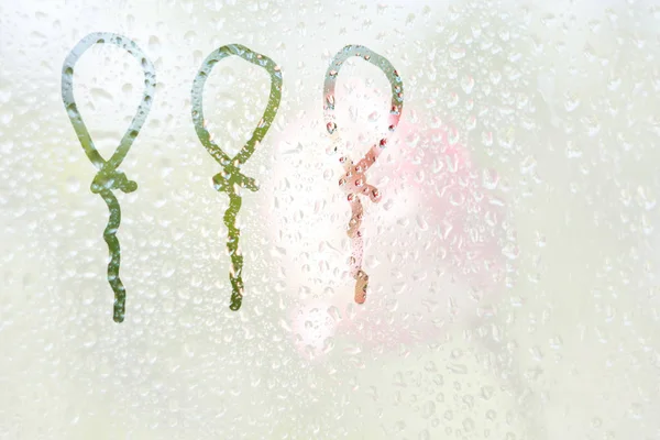 在半透明的雾玻璃上画一个手指形状的气球条纹。春雨雨滴在窗户特写上。模糊的背景，复制空间。庆祝 — 图库照片