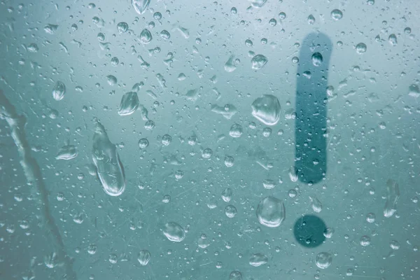 A finger drawing of the shape of an exclamation mark stripe on a semitransparent foggy glass. raindrops of spring rain on the window close-up. blurred background copy space