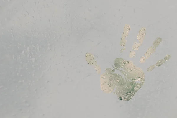 Der Abdruck einer menschlichen Handfläche auf einem durchscheinenden, vernebelten Glas. Frühlingsregen tropft aus nächster Nähe auf vernebelte Fenster. verschwommener Hintergrundkopierraum — Stockfoto