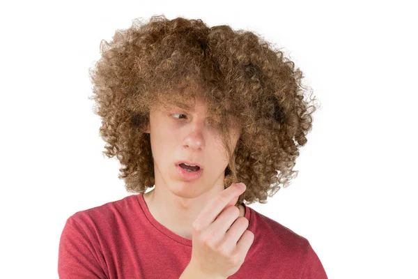 Portrait d'un jeune homme européen frisé effrayé regarde ses cheveux longs. tient une boucle de cheveux avec ses doigts. cheveux masculins très luxuriants. cheveux bouclés pour les hommes. isolé sur fond blanc — Photo