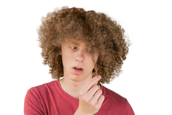 Retrato de um jovem encaracolado europeu homem assustado olha para o seu cabelo longo. segura um fio de cabelo com os dedos. cabelo masculino muito exuberante cara. cabelo ondulação para os homens. isolado em fundo branco — Fotografia de Stock