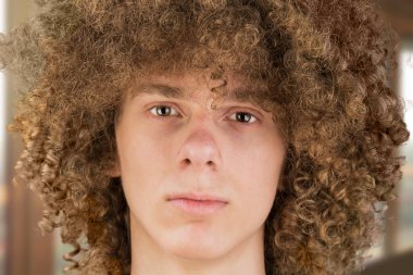 Uzun kıvırcık saçlı, cüretkar bakışlı genç Avrupalı bir adamın portresi çerçeveye yakın plan bulanık arka plana bakıyor. Bir erkekten çok gür erkek saçı. Bir tutku kilidi