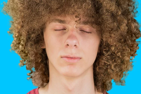 Cropped portrait of a young curly European man with long curly hair and closed eyes close up against blue background. very lush male hair. curling hair for men. a lock of passion — Stock Photo, Image