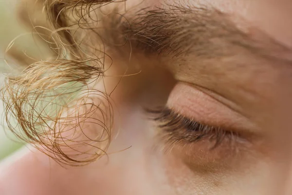 male eye close up. a curl of curly hair hangs over a man\'s face. thoughtful look into the void