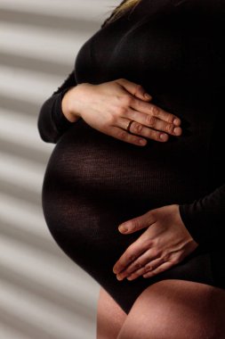 Hamileliğinin dokuzuncu ayında büyük göbekli hamile bir kadın karnına sarılıyor. Doğum beklentisiyle.