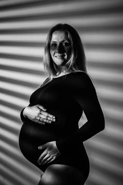 妊娠9ヶ月目に大きな腹を持つランジェリー姿の妊婦さんが5本星の隣にポーズをとっています。出産を見越して — ストック写真