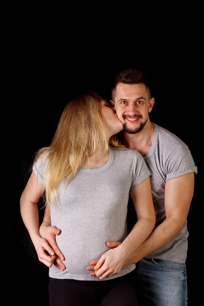 Hamileliklerinin dokuzuncu ayında olan bir erkek ve hamile bir kadın izole edilmiş bir siyah arka plana sarılıyorlar. Ailede takviye bekliyor. — Stok fotoğraf