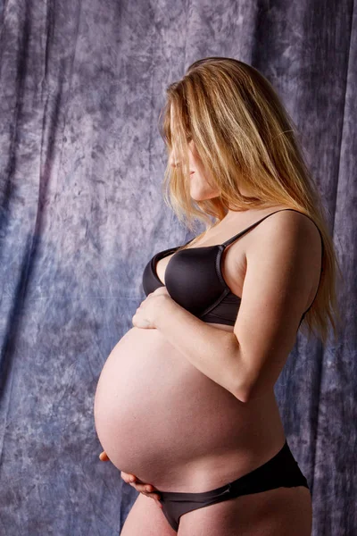 Een zwangere vrouw in lingerie met een dikke buik in de negende maand van de zwangerschap knuffelt haar buik. in afwachting van de bevalling Stockafbeelding