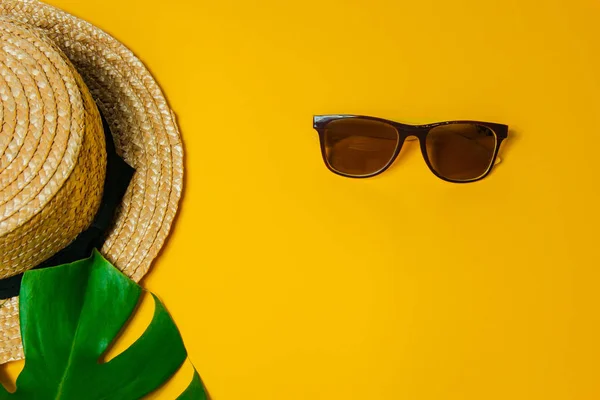 Αξεσουάρ παραλίας: ψάθινο καπέλο, γυαλιά ηλίου και μεγάλα φύλλα τέρατα φυτά για σκιά σε ένα φωτεινό κίτρινο φόντο σε μια ηλιόλουστη μέρα, επάνω όψη, αντίγραφο χώρου — Φωτογραφία Αρχείου