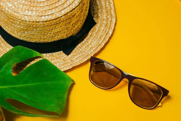 Αξεσουάρ παραλίας: ψάθινο καπέλο, γυαλιά ηλίου και μεγάλα φύλλα τέρατα φυτά για σκιά σε ένα φωτεινό κίτρινο φόντο σε μια ηλιόλουστη μέρα, επάνω όψη, αντίγραφο χώρου — Φωτογραφία Αρχείου
