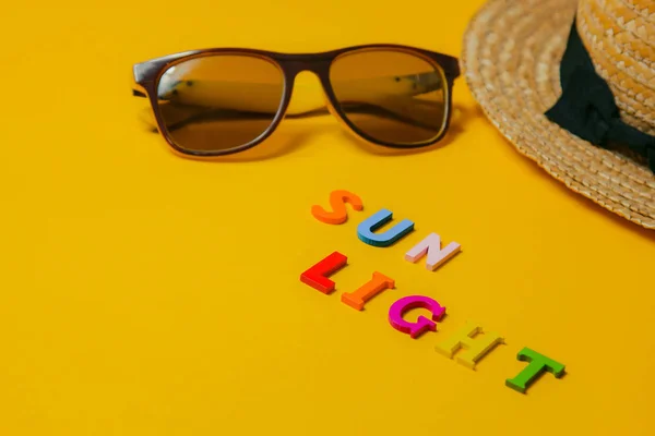 Έννοια της χαλάρωσης στο φως του ήλιου στην παραλία. επιγραφή Sunlight σε κίτρινο φόντο μαζί με γυαλιά ηλίου και ψάθινο καπέλο. πάνω όψη — Φωτογραφία Αρχείου