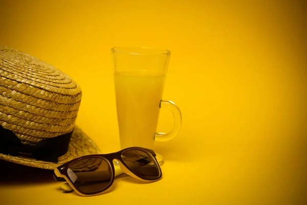Έννοια της χαλάρωσης και της δίψας στην παραλία. ένα ποτήρι λεμονάδα σε κίτρινο φόντο με γυαλιά ηλίου και ψάθινο καπέλο. πάνω όψη — Φωτογραφία Αρχείου