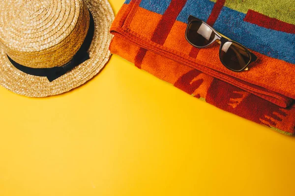 concept of relaxing on the beach. beach set on a yellow background with sunglasses, towel and straw hat. top view