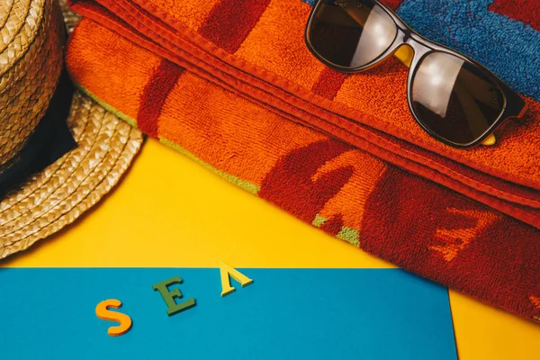 Έννοια της χαλάρωσης στην παραλία. επιγραφή θάλασσα σε κίτρινο φόντο με γυαλιά ηλίου, μια πετσέτα και ένα ψάθινο καπέλο. πάνω όψη — Φωτογραφία Αρχείου