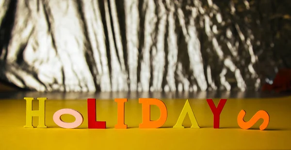 inscription holidays from colorful bright wooden letters lie on a bright background