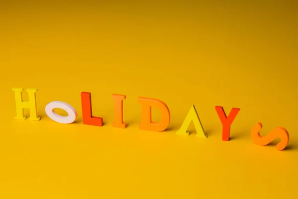 Napis wakacje z kolorowych jasnych liter drewnianych leżą na jasnym żółtym tle góry widok miejsca kopiowania — Zdjęcie stockowe