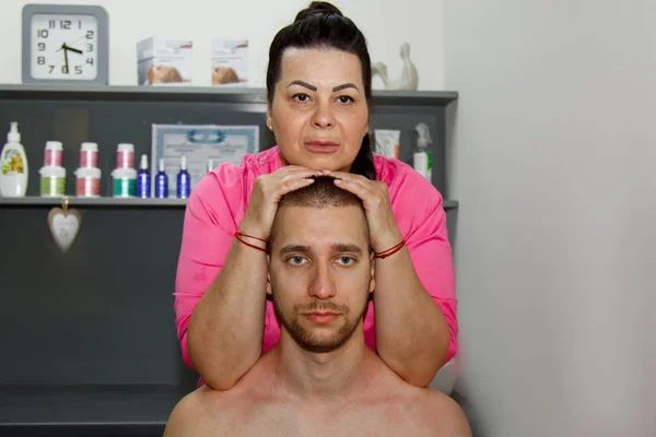 プロの治療の首および頭部のマッサージ。マッサージルームでアスリートを男に痛みの回復手順。若い患者に対する操作的脊椎治療を行う女性理学療法士 — ストック写真
