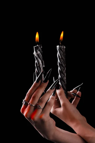 Female hands with long nails hold burning candles on a black isolated background. concept of witchcraft witchcraft on halloween. silver rings on the fingers — Stock Photo, Image
