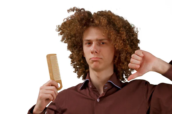 Retrato de um jovem de cabelos encaracolados com um pente de madeira no cabelo magnífico insatisfeito com o resultado em um fundo isolado branco. conceito de cuidado do cabelo masculino — Fotografia de Stock