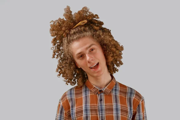 Retrato de um jovem de cabelos encaracolados com um pente de madeira no cabelo cheio sorrindo em um fundo isolado cinza. conceito de cuidado do cabelo masculino — Fotografia de Stock