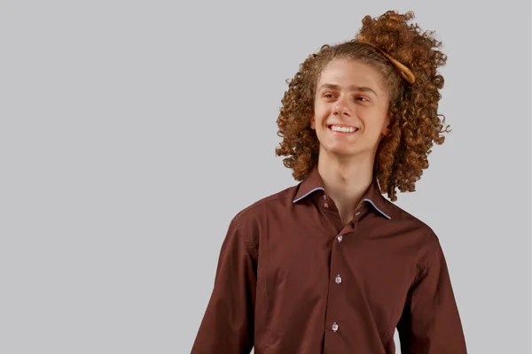 Portrait of a curly-haired young man with a wooden comb in full hair smiling on a gray isolated background. male hair care concept — Stock Photo, Image