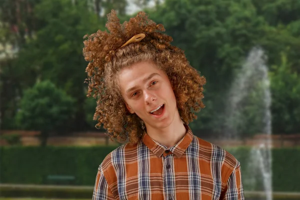 Портрет кудрявого молодого человека с деревянной расчёской в полных волосах, улыбающегося на фоне парка. мужской уход за волосами — стоковое фото