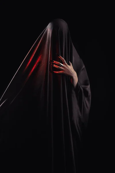 woman covered with black cloth stands on an isolated black background. faceless death concept