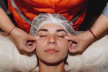 spa uzmanı tıbbi şapkalı genç bir kıza yüz masajı yapıyor. güzellik bakımları yakın çekim