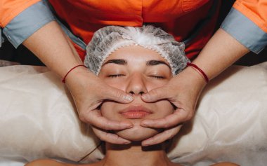 spa uzmanı tıbbi şapkalı genç bir kıza yüz masajı yapıyor. güzellik bakımları yakın çekim