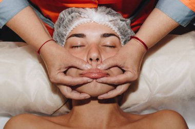 spa uzmanı tıbbi şapkalı genç bir kıza yüz masajı yapıyor. güzellik bakımları yakın çekim