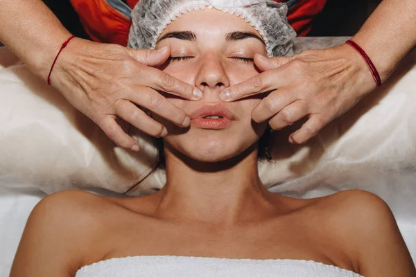 Especialista en spa está haciendo masaje facial a una joven con una gorra médica. tratamientos de belleza de cerca — Foto de Stock