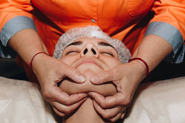 Wellness-Spezialist macht Gesichtsmassage für ein junges Mädchen mit medizinischer Mütze. Schönheitsbehandlungen aus nächster Nähe — Stockfoto