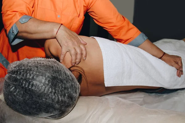 Ein Wellness-Spezialist verdreht einem jungen Mädchen in medizinischer Mütze die Wirbelsäule. Körperliche Eingriffe aus nächster Nähe. Erholung von Rückenschmerzen — Stockfoto