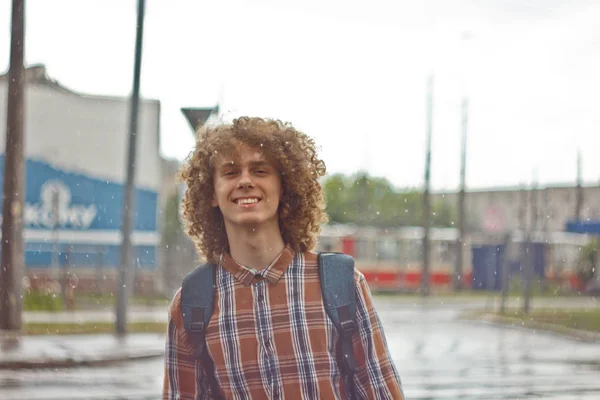 Göndör hajú fiatal srác áll az utcán egy táska a vállán. és fiatal utazó koncepcióját. portréja egy fiatal férfi — Stock Fotó