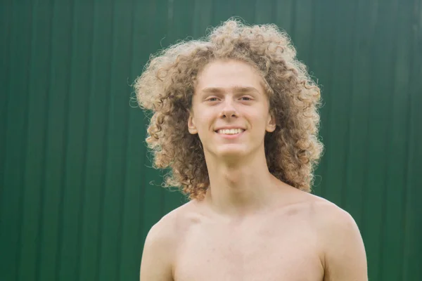 Portrait of a young curly-haired guy on the street against a green fence. topless young man — Stock Photo, Image