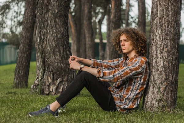 Portrait of a young curly-haired guy in a summer park on the street. student and young traveler concept — Stock Photo, Image