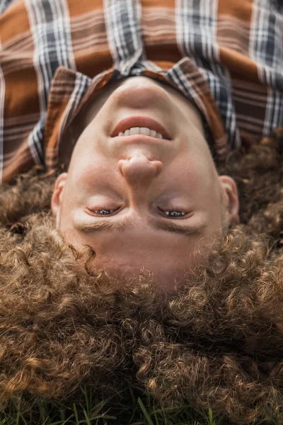 Curly-haired jonge kerel ligt op de straat op de begane top uitzicht. student en jong reiziger concept. Portret van een jongeman — Stockfoto
